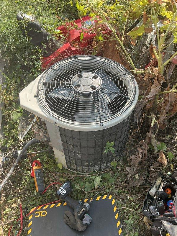 Responded to cooling system complaint and performed diagnostic evaluation of residential HVAC system. Inspected outdoor condensing unit, which was found heavily obstructed by overgrown vegetation and debris affecting proper airflow and heat dissipation. Assessed indoor furnace unit located in basement crawl space with dirt floor. Documented equipment conditions through photographic documentation for service records. System evaluated for age, brand identification, and operational status to determine appropriate repair recommendations.