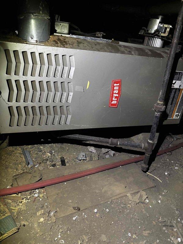 Responded to cooling system complaint and performed diagnostic evaluation of residential HVAC system. Inspected outdoor condensing unit, which was found heavily obstructed by overgrown vegetation and debris affecting proper airflow and heat dissipation. Assessed indoor furnace unit located in basement crawl space with dirt floor. Documented equipment conditions through photographic documentation for service records. System evaluated for age, brand identification, and operational status to determine appropriate repair recommendations.