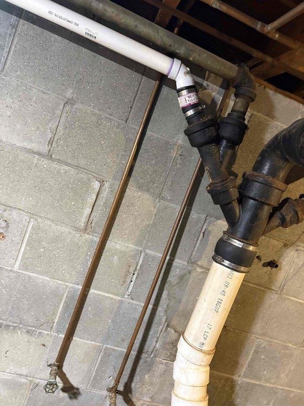 Conducted comprehensive plumbing assessment for whole house re-piping project. Documented existing plumbing infrastructure in basement utility area, including aged metal fittings, PVC piping sections, shut-off valves, and copper support brackets mounted to concrete block foundation walls. Photographed exposed ceiling joists, metallic ductwork, and current pipe routing to develop accurate scope of work for complete residential plumbing system replacement.