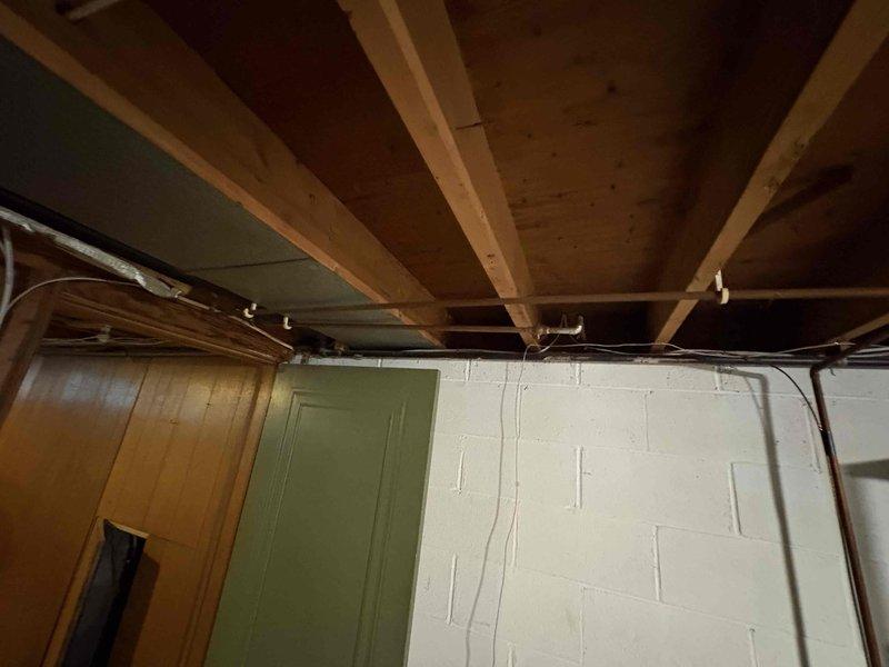 Conducted comprehensive plumbing assessment for whole house re-piping project. Documented existing plumbing infrastructure in basement utility area, including aged metal fittings, PVC piping sections, shut-off valves, and copper support brackets mounted to concrete block foundation walls. Photographed exposed ceiling joists, metallic ductwork, and current pipe routing to develop accurate scope of work for complete residential plumbing system replacement.