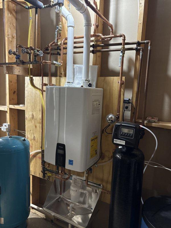 Successfully completed installation of new furnace and tankless water heater system in residential mechanical space. Mounted Energy Star certified tankless water heater unit to wall framing with complete copper piping connections including multiple supply and return lines with appropriate shut-off valves. Installed furnace system with vertical air handler assembly and connected metallic ductwork for proper air distribution throughout the home. Integrated existing water treatment equipment including pressure expansion tank and water softener system into new plumbing configuration. All copper piping routed systematically with proper spacing for maintenance access. Electrical connections completed with appropriate panel integration. System installed on proper base platform with all components positioned for optimal performance and serviceability. Installation verified operational and ready for use.
