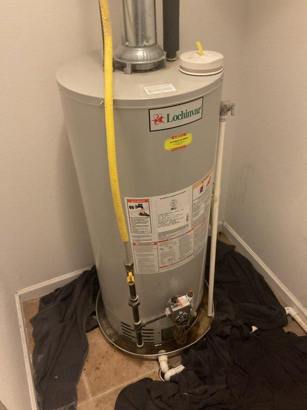 Responded to service call for leaking water heater. Upon arrival, inspected 6-year-old Lochinvar residential water heater installed in utility closet. Identified active leak at base of unit near plumbing connections. Examined all visible components including yellow flexible gas line, PVC discharge piping, brass fittings, temperature and pressure relief valve, and gas control assembly. Documented equipment condition with photographs showing overall installation, venting configuration with metallic flue pipe, and connection points. Based on age of unit and location of leak, recommended water heater replacement as most cost-effective solution.