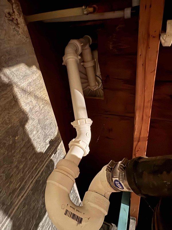 Responded to basement plumbing leak caused by drainage blockage. Inspected PVC pipe configuration beneath wooden structure and under-sink trap assembly, identifying compromised drainage system with multiple elbow joints and fittings. Cleared blockage from drain line, verified proper flow through U-trap configuration, and confirmed all connections were secure with no active leaks. Documented existing plumbing layout including PVC drainage pipes, copper fittings, and cast iron components for service records.
