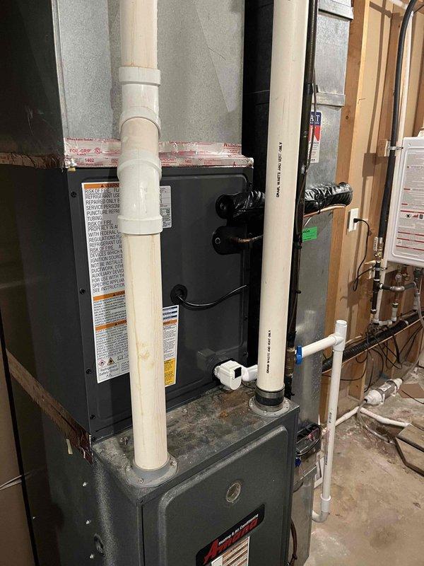 Completed full HVAC system replacement including indoor furnace unit and outdoor condensing unit. Installed new furnace in basement utility area with proper ventilation using white PVC piping, including elbows and drainage connections. Mounted unit on gray plenum base with all safety labels and specifications clearly visible. Routed black refrigerant lines from indoor unit to outdoor condenser. Installed new outdoor AC condensing unit on concrete pad with proper clearances, connected via gray PVC electrical conduit to wall-mounted disconnect box. Verified all electrical connections, refrigerant line sets, and drainage systems functioning properly. System tested and operational upon completion.