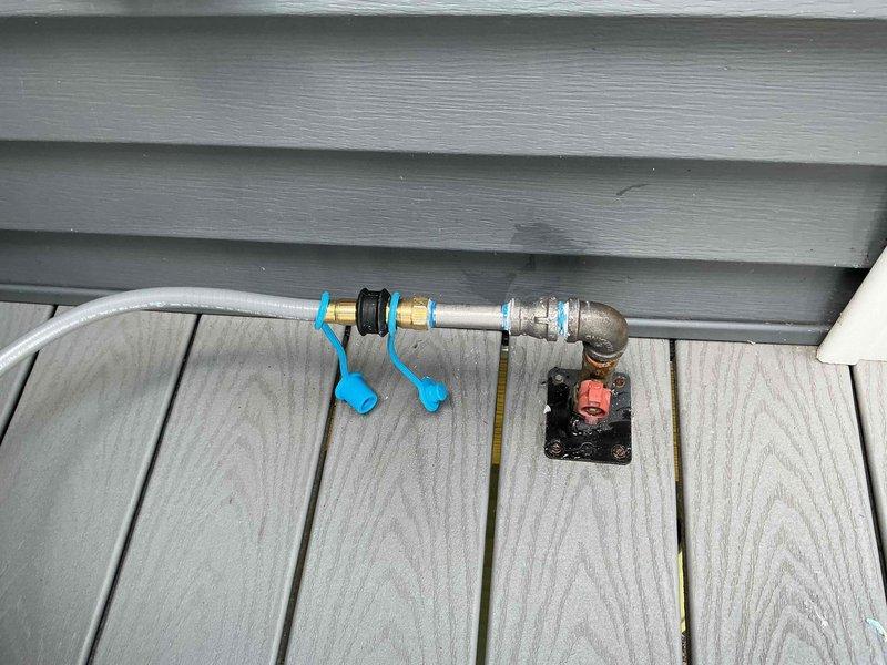 Assessed existing natural gas deck shut-off valve and plumbing infrastructure for connection to new Weber Spirit natural gas grill at condo unit. Evaluated brass fittings, mounting brackets, and valve assembly currently installed on exterior siding above composite deck to determine compatibility and connection requirements for grill installation. Documented existing gas line configuration including white PVC transition to metallic piping with L-shaped descent to shut-off valve mechanism.