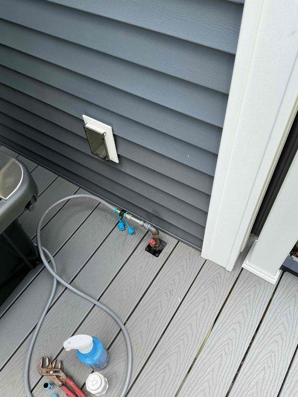 Assessed existing natural gas deck shut-off valve and plumbing infrastructure for connection to new Weber Spirit natural gas grill at condo unit. Evaluated brass fittings, mounting brackets, and valve assembly currently installed on exterior siding above composite deck to determine compatibility and connection requirements for grill installation. Documented existing gas line configuration including white PVC transition to metallic piping with L-shaped descent to shut-off valve mechanism.