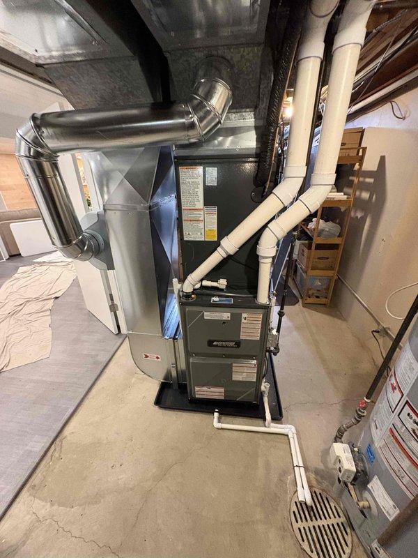 Completed full HVAC system installation including new furnace and air conditioning condenser unit. Installed gray furnace unit in basement utility area with proper metallic ductwork connections to existing air distribution system. Mounted beige/tan outdoor AC condenser on concrete pad in backyard with appropriate clearances. Ran and secured white PVC condensate drain and vent piping along exterior brick wall and interior basement area. Connected all electrical components, refrigerant lines, and ductwork transitions per manufacturer specifications. Verified proper airflow, tested system operation, and confirmed both heating and cooling functions operating within normal parameters.