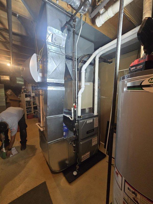 Completed full furnace installation in basement utility room. Installed new gray metal furnace unit with proper positioning and clearances alongside existing water heater and HVAC components. Ran and secured white PVC venting and condensate drain piping vertically and horizontally through ceiling joists. Connected metallic ductwork including cylindrical and rectangular sections with proper sealing at all joints and seams. Installed flexible ductwork routing through ceiling structure for air distribution. Verified all connections, tested system operation, and confirmed proper drainage function. Unit operational and ready for service.
