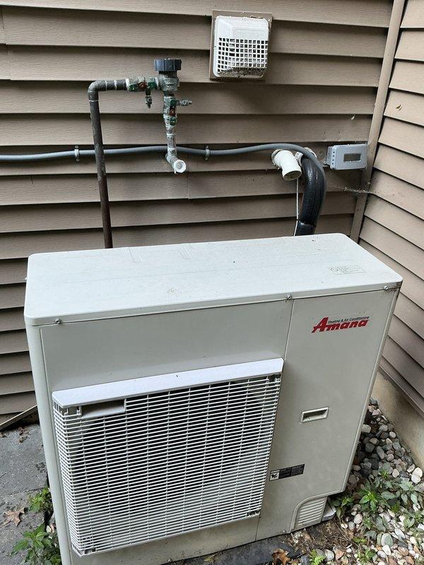 Completed annual cooling maintenance on 2021 Amana heat pump system. Performed comprehensive tune-up including inspection of outdoor condensing unit, refrigerant lines, and associated components. Verified proper operation of all electrical connections, drainage system with PVC condensate lines, and copper refrigerant piping showing normal weathering patina. Unit operating within manufacturer specifications with adequate airflow through condenser coil and proper clearance around equipment on concrete pad.