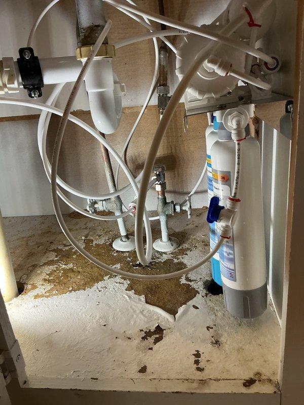 Completed installation of reverse osmosis water filtration system under kitchen sink. System includes multiple-stage filtration with vertical filter cartridges, pressure tank, feed water connections, and drain line with all necessary valves and fittings properly installed and secured using flexible tubing connections. All components tested and operational upon completion.