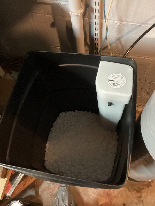 Responded to plumbing leak at newly installed water softener with progressive water accumulation at base unit. Upon inspection, identified leak source in overhead plumbing connections. Tightened brass fittings and valve connections on supply lines, verified proper sealing at all threaded joints. Installed drain pan with absorbent pad and water sensor alarm beneath unit as preventative measure. Tested system under pressure, confirmed leak resolved with no further water discharge. Advised monitoring for 24-48 hours to ensure complete resolution.
