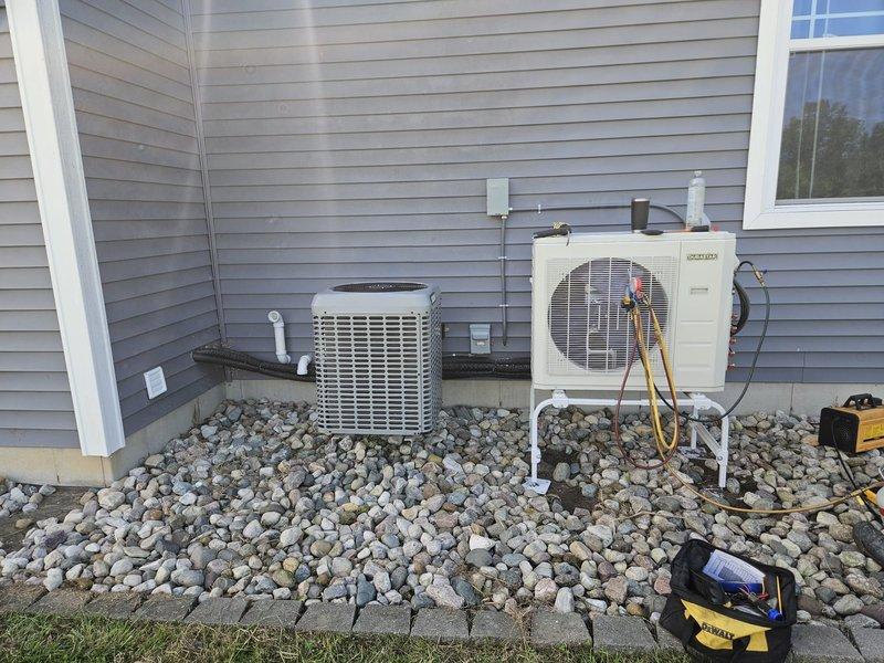 Completed installation of multi-zone ductless mini-split system including two outdoor condensing units mounted on prepared rock bed with proper drainage and electrical connections. Installed indoor wall-mounted air handler unit in interior space with refrigerant line sets, condensate drainage, and electrical wiring routed through building structure. System tested and verified operational upon completion.