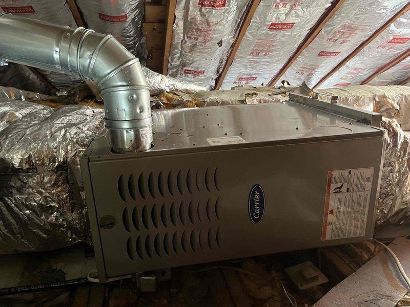 Completed full furnace installation in attic space, including horizontal Carrier unit mounted on wooden platform with proper clearances. Connected rigid galvanized metal supply ductwork with elbow transition to existing distribution system and verified all flexible duct connections were secure. Installation performed in accordance with manufacturer specifications with unit positioned for optimal airflow and serviceability within the insulated attic environment.