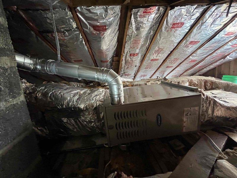 Completed full furnace installation in attic space, including horizontal Carrier unit mounted on wooden platform with proper clearances. Connected rigid galvanized metal supply ductwork with elbow transition to existing distribution system and verified all flexible duct connections were secure. Installation performed in accordance with manufacturer specifications with unit positioned for optimal airflow and serviceability within the insulated attic environment.