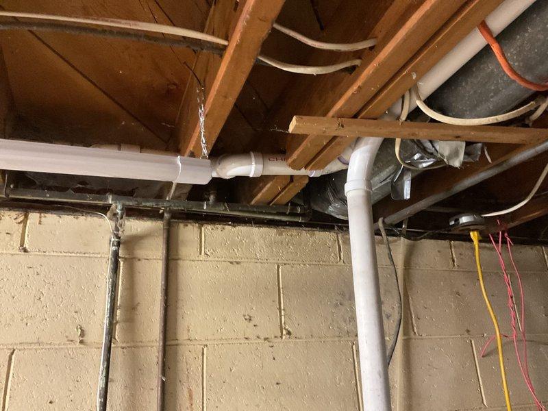 Responded to drainage complaint where washing machine discharge was backing up into kitchen sink. Upon inspection, accessed basement plumbing system and identified improper drain line configuration in the washing machine standpipe connection. The issue was caused by inadequate venting and potential partial blockage in the shared drain line between the laundry and kitchen fixtures.

Examined the PVC drainage system running through the basement ceiling joists and confirmed the washing machine drain was improperly tied into the kitchen sink drain line without proper venting, creating a siphoning effect during wash cycles. Verified sump pump operation and checked all visible drain connections for proper pitch and secure fittings. Cleared the affected drain line and confirmed proper water flow from both the washing machine and kitchen sink. System now draining properly with no backup issues observed during testing.