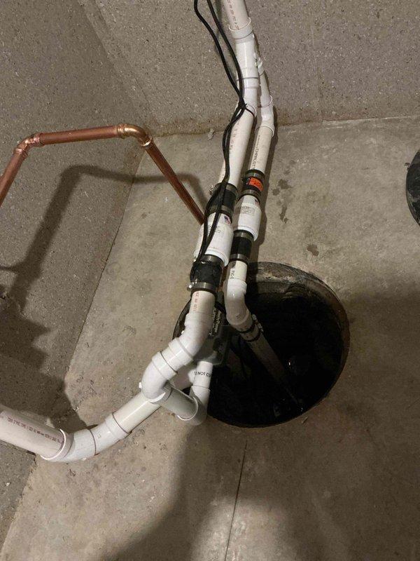 Completed installation of backup sump pump system with associated plumbing connections. Installed sump basin in concrete floor with converging PVC drainage lines and copper water supply piping, secured electrical wiring to discharge lines, and integrated system with existing basement infrastructure to provide redundant water removal capability.