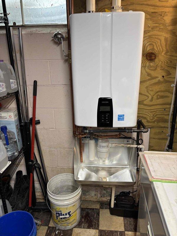 Completed installation of wall-mounted tankless water heater unit in utility area. Connected copper supply and discharge piping to unit, installed gas control valve assembly with flexible gas line, and secured all connections with proper mounting hardware. Installed condensate collection pan beneath unit and routed white PVC exhaust venting through exterior wall. Verified proper operation of digital control panel, tested all plumbing connections for leaks, and confirmed unit achieved proper temperature output and flow rate per manufacturer specifications.