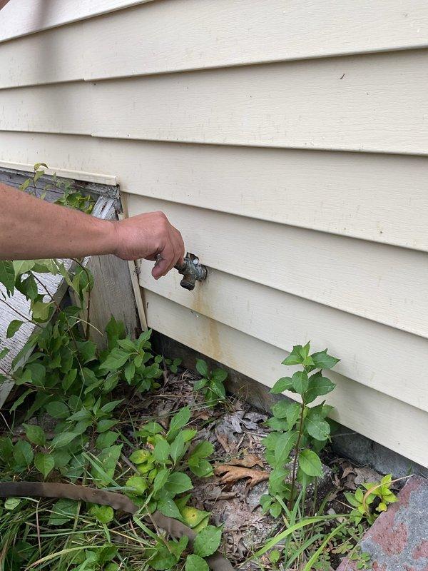 Responded to a plumbing leak complaint involving an exterior hose bib and its associated supply valve in the basement. Upon inspection, identified active leaking at the outdoor spigot mounted on the home's exterior siding, with visible water staining present below the fixture. Traced the water supply line to the basement utility area where the connecting shut-off valve was also found to be leaking. The basement environment showed evidence of long-term moisture exposure with deteriorated concrete block walls, corroded plumbing components, and water damage throughout the space. Assessed the condition of copper supply piping running vertically along the foundation wall, noting corrosion and age-related deterioration of various plumbing connections in the area. Documented both leak locations with photographs showing the exterior spigot condition and the basement valve assembly. Provided recommendations for repair or replacement of both the outdoor hose bib and the interior supply valve to 