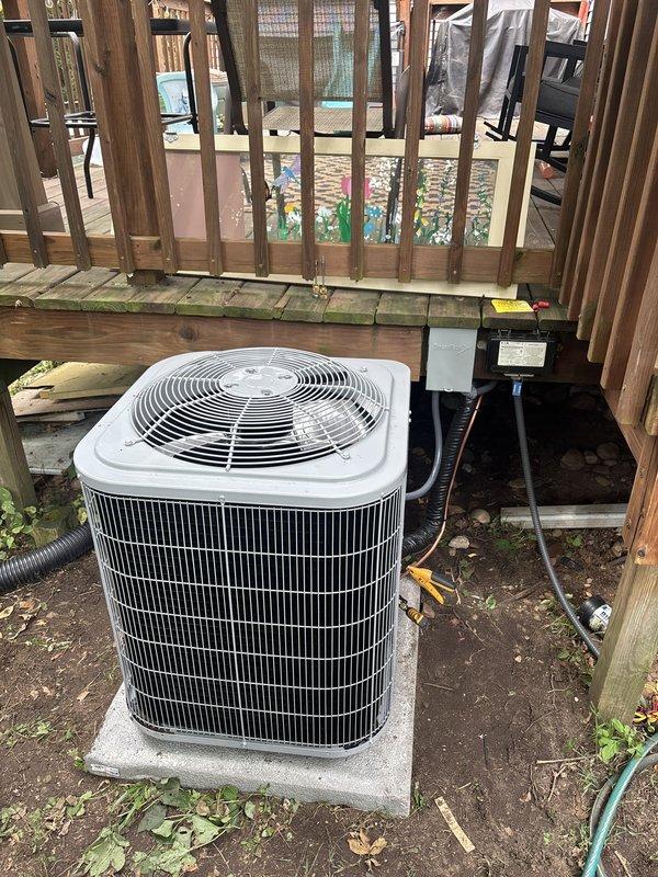 Completed full installation of new furnace and air conditioning system at residential property. Outdoor condenser unit was positioned on concrete pad beneath elevated deck structure with proper electrical disconnect box installed and all refrigerant lines connected. System was charged with refrigerant per manufacturer specifications, with initial charge of 39 pounds and additional 6 ounces added to achieve optimal operating levels. All electrical connections, copper line sets, and condensate drainage were installed to code, and unit was tested for proper operation and cooling performance.