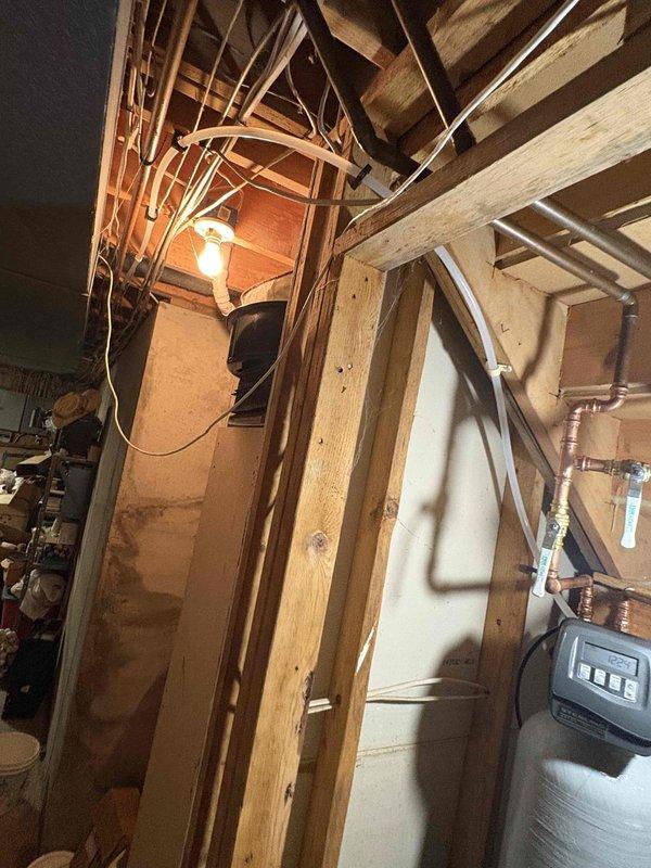Completed installation of water softener system in basement utility area. Installed white cylindrical softener tank with insulated wrap, mounted gray digital control head with display panel, and connected copper supply lines from overhead joists to system with proper fittings and valves. Positioned brine tank receptacle on floor adjacent to softener unit and verified all plumbing connections for proper operation.