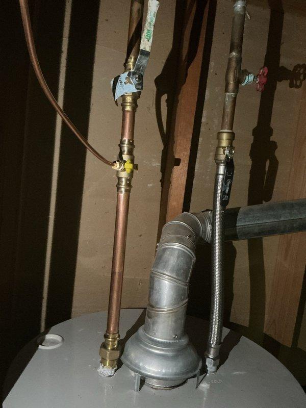 Completed installation of replacement humidifier unit with manual control in residential basement mechanical room. The new white humidifier unit was mounted adjacent to the existing green furnace and connected to the HVAC ductwork via flexible tubing. Installation included integration with the home's plumbing system, utilizing existing copper supply lines and brass fittings visible near the water heater assembly. All connections were secured, system was tested for proper operation, and the unit is now fully functional to provide whole-home humidity control.