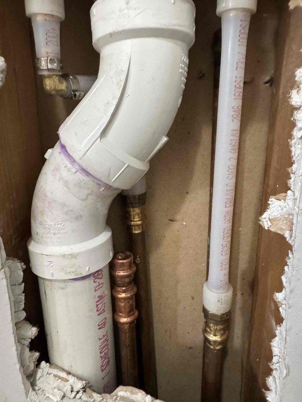 Completed laundry box repair involving exposed plumbing installation within wall cavity. Accessed and repaired connections between white PVC drainage pipes and copper water supply lines, including elbow joint fittings and flexible supply lines with brass compression fittings. Verified GFCI outlet functionality and secured all plumbing connections within the wall structure. Work completed within the quoted 3-hour timeframe with customer waiting on-site.