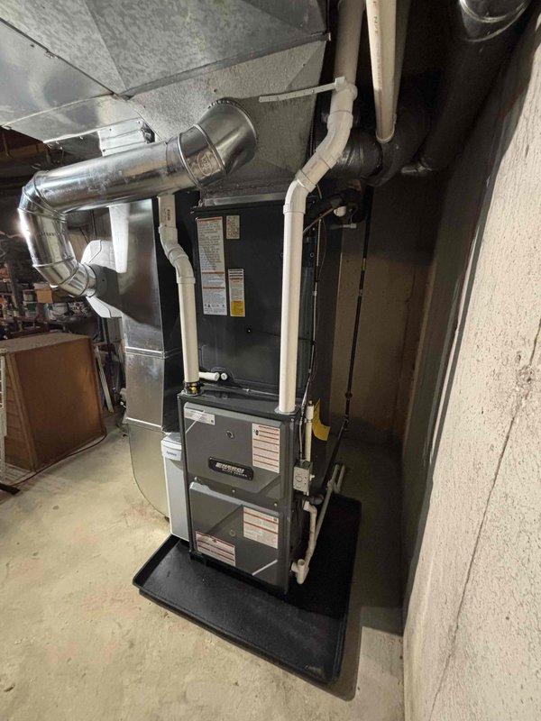 Completed full HVAC system installation including new furnace and air conditioning condenser unit. Furnace installed in basement utility area with proper ductwork integration, PVC venting, and condensate drainage system on protective drain pan. Outdoor AC condenser unit positioned on concrete pad with landscaping rock bed, electrical disconnect box mounted, and all refrigerant lines connected and tested for proper operation.