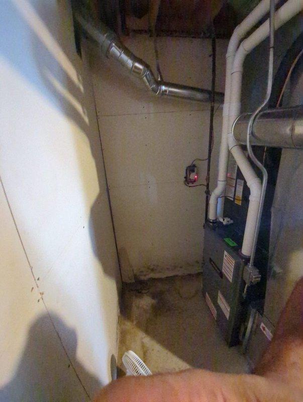 Completed full air conditioning system replacement at residential property. Removed existing outdoor condenser unit and installed new dark gray AC condenser on existing concrete pad along side of house near utility connections. Unit positioned in narrow access area between foundation and landscaping with proper clearance for airflow and service access. Verified all refrigerant line connections, electrical hookups, and drainage systems functioning properly. Confirmed indoor air handler integration with existing furnace and ductwork in basement mechanical room. All metallic ductwork connections inspected and secured. System tested for proper operation, temperature differential, and refrigerant charge levels. Unit operating within manufacturer specifications upon completion.