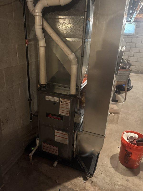 Completed full furnace installation in basement utility area. Installed new Amana gas furnace unit on protective base pad with proper venting system including PVC exhaust pipes and ductwork connections. Connected gas line, electrical conduit, and silver supply/return ductwork to ensure complete system integration and proper airflow throughout the residence.