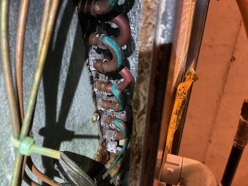 Responded to no cooling complaint on 15-year-old air conditioning system. Upon arrival, performed diagnostic inspection of the unit and associated components. Documented existing conditions including significantly corroded copper refrigerant lines and fittings showing advanced oxidation with green patina formation, indicating extended exposure to moisture and age-related deterioration. Observed water staining and rust streaks on internal metal panels near pipe connections, suggesting potential historical moisture intrusion. Photographed deteriorated plumbing connections, corroded pipe assemblies, and overall system condition for documentation purposes.