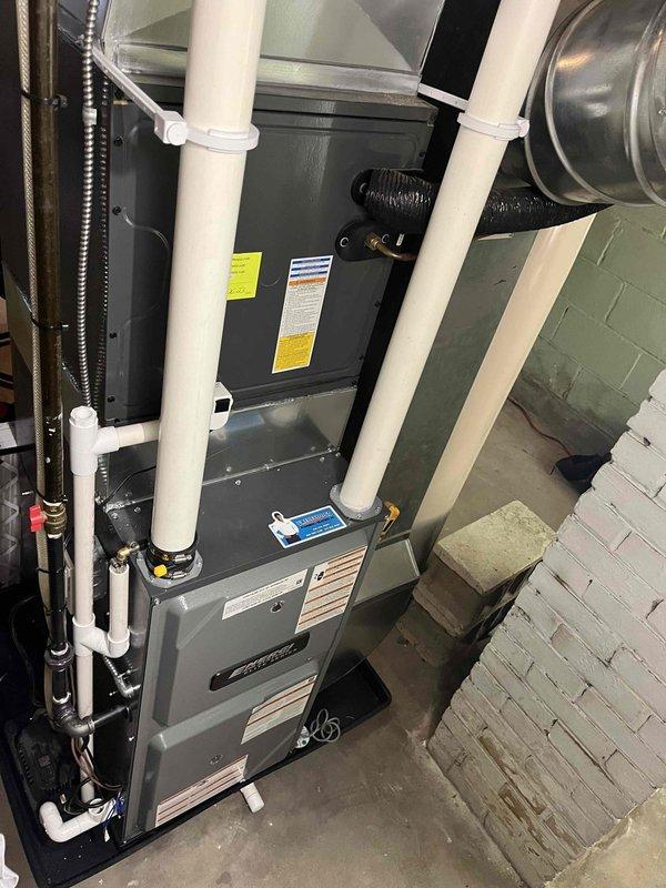 Completed full furnace installation in basement utility area. Installed new forced-air heating system with proper venting configuration using white PVC intake and exhaust pipes, connected metallic ductwork and flexible ducting to distribution system, and positioned evaporator coil assembly for integration with existing air conditioning components. System tested and confirmed operational with all safety labels and specifications visible, air filter properly installed, and all electrical and gas connections secured per manufacturer requirements.