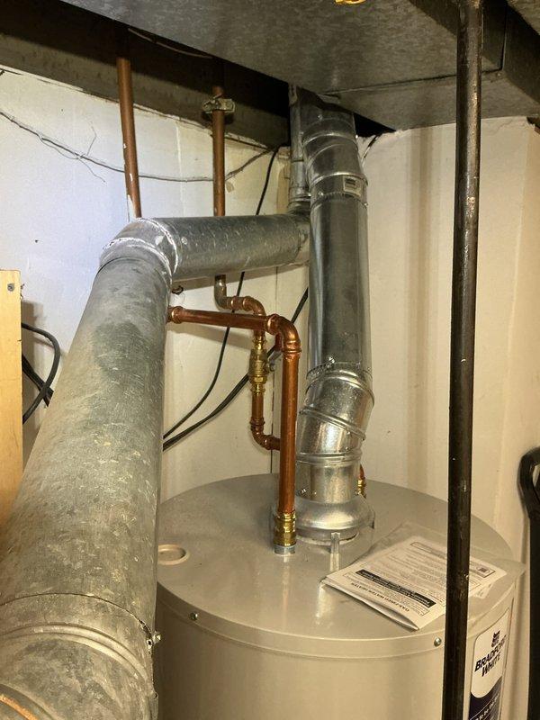 Responded to water leak service call where condensation drain line was actively leaking in the mechanical space. Upon inspection, identified compromised condensation drain line requiring attention to prevent continued water damage. Additionally observed that the galvanized flue pipe exhibited deteriorated seam joints showing signs of age, oxidation, and separation that required sealing work to ensure proper venting and prevent potential safety hazards. The flue pipe displayed significant weathering with visible surface corrosion and mottled patina throughout the ductwork sections. Documented existing conditions of HVAC system components including aged galvanized ductwork with riveted seams, copper refrigerant lines showing oxidation, and water heater installation with associated plumbing connections. System age could not be determined from available information on equipment. Photographed condensation drain line leak location and flue pipe seam deterioration for service records and futu