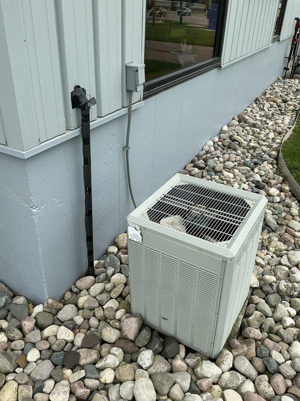 Performed comprehensive estimate for non-operational residential air conditioning system with ground-level outdoor condensing unit and basement furnace installation. Documented existing equipment conditions including beige condensing unit positioned on river rock landscaping bed against exterior wall, and basement furnace with multiple insulated ductwork configurations in black and silver wrapping. Assessed system components, photographed equipment placement and mechanical connections, and prepared detailed estimate for repair or replacement options to restore cooling functionality.