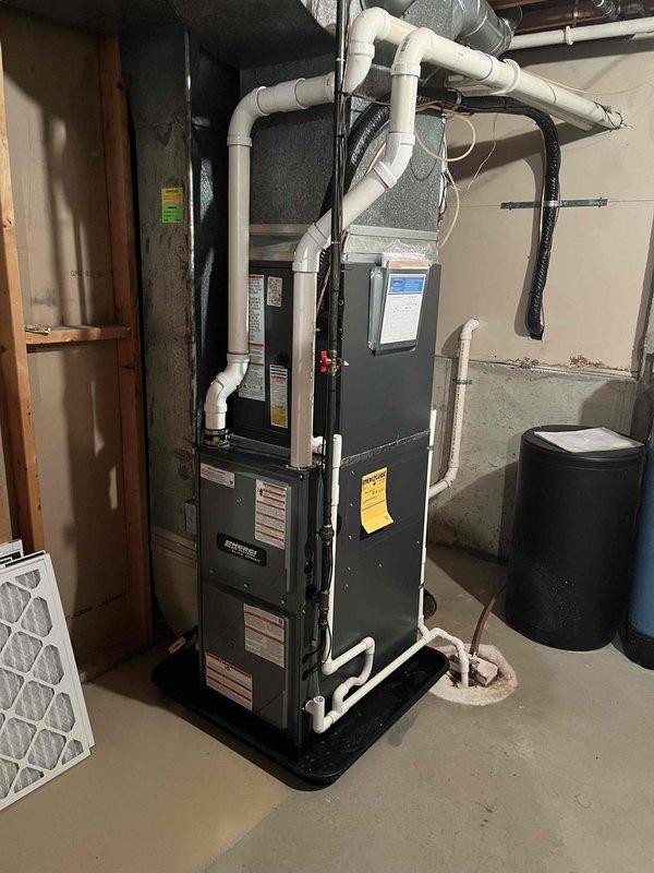 Completed full HVAC system replacement including outdoor condensing unit and indoor air handler/furnace. Removed existing equipment and installed new dark-colored condensing unit on existing concrete pad with proper refrigerant line sets, electrical disconnect, and PVC line hide. All refrigerant lines professionally routed up exterior wall with white line set covers for clean appearance. Indoor unit installed in basement utility area with new PVC venting system routed to exterior, secured with appropriate clamps and hangers. Connected all electrical components including disconnect box mounted to exterior wall per code requirements. System positioned on decorative river rock base with landscape edging for drainage and aesthetics. Completed all refrigerant connections, pressure tested system, evacuated lines, and charged to manufacturer specifications. Verified proper electrical connections, tested all safety controls, and confirmed system operation through complete heating and cooling c