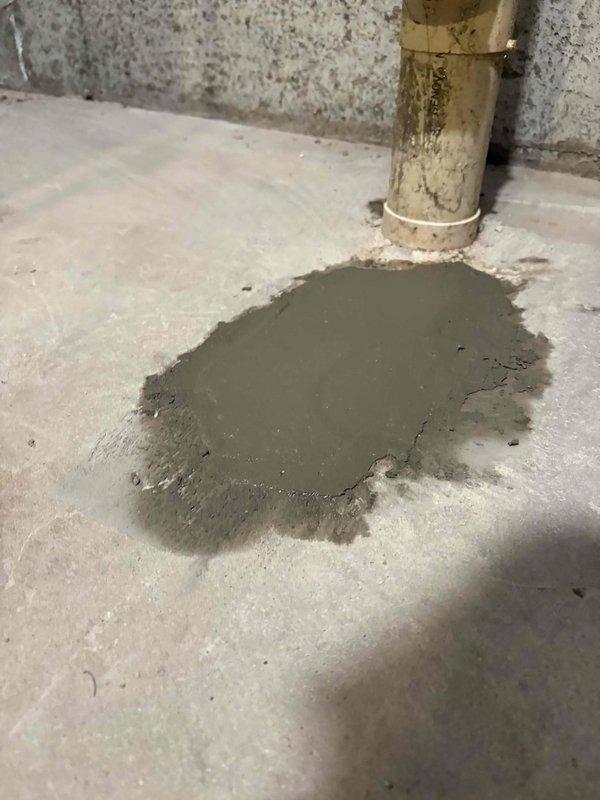 Responded to standing water issue in basement utility area. Poured and applied fresh concrete/cement around brass pipe base to seal floor penetration and prevent water infiltration. Completed repair work around floor drain area where moisture accumulation was evident.
