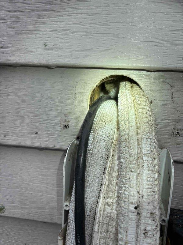 Responded to water leak complaint on Fujitsu mini split system. Upon inspection, found deteriorated foam insulation on refrigerant line set with significant gap allowing condensate accumulation and dark debris buildup around exposed piping. Documented condition of both interior insulated piping and exterior wall penetration where line set passes through siding, noting aged and discolored insulation requiring replacement to prevent continued moisture issues.