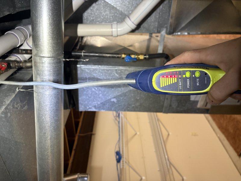 Responded to gas leak call near furnace location. Upon arrival, utilized refrigerant leak detector with flexible probe to systematically inspect HVAC components, ductwork, and gas line connections in mechanical area. Identified leak at flexible corrugated gas line connection point near furnace. Inspected associated plumbing components, PVC piping, and metal fittings in the vicinity. Applied leak detection solution to verify exact location of gas escape at connection fitting. Documented conditions with photographs for service records.