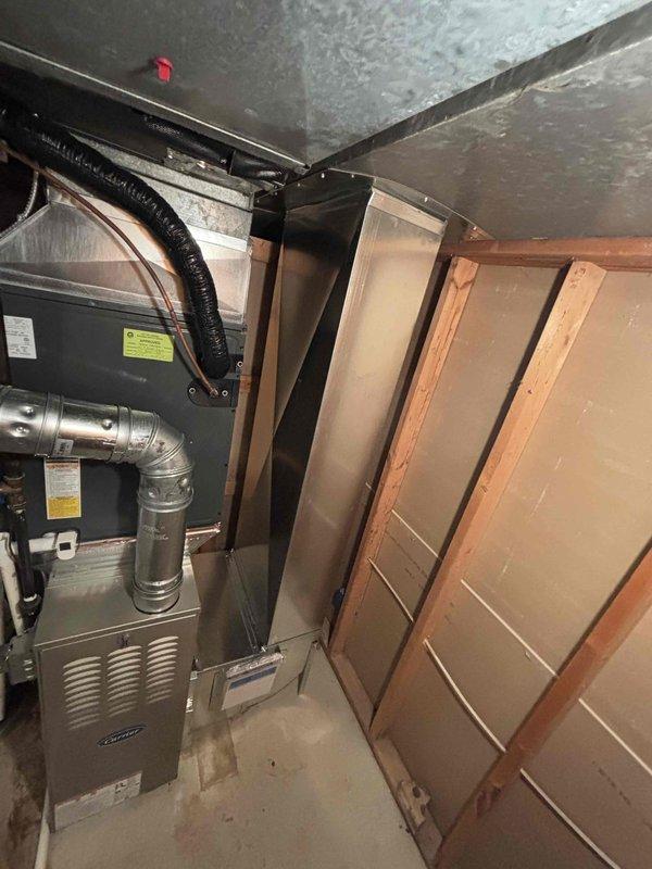 Successfully completed furnace installation in basement utility area. Installed new gray metal furnace unit with proper connections to existing ductwork system, including silver flexible and rigid metallic supply ducts. Ensured all ductwork connections were properly secured and sealed, with black flexible conduit routing completed. Unit positioned adjacent to existing water heater with adequate clearance for service access and proper ventilation. All manufacturer specifications followed for installation, including gas line connections, electrical hookup, and venting requirements. System tested and verified operational.
