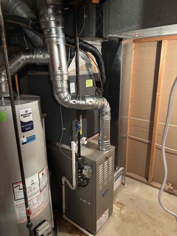 Successfully completed furnace installation in basement utility area. Installed new gray metal furnace unit with proper connections to existing ductwork system, including silver flexible and rigid metallic supply ducts. Ensured all ductwork connections were properly secured and sealed, with black flexible conduit routing completed. Unit positioned adjacent to existing water heater with adequate clearance for service access and proper ventilation. All manufacturer specifications followed for installation, including gas line connections, electrical hookup, and venting requirements. System tested and verified operational.