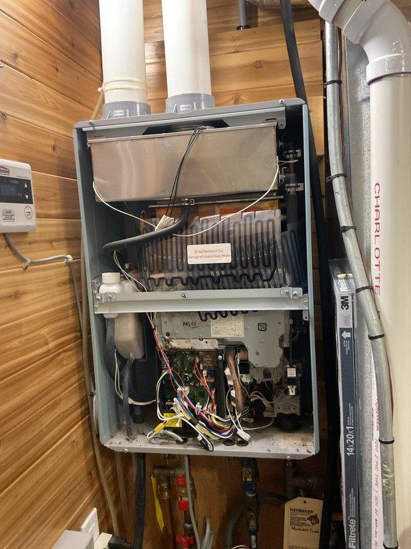 Responded to service call for 8-year-old Richmond tankless water heater with no hot water production. Upon arrival, accessed unit's internal components by removing front panel to diagnose heating failure. Inspected heat exchanger assembly, control board, electrical connections, and wiring harness for potential faults. Examined venting system including intake and exhaust PVC piping for proper configuration and blockages. Documented internal component condition including circuit board, wire connections, and heat exchanger coils through photographic evidence. Completed diagnostic assessment of non-operational tankless water heating system.