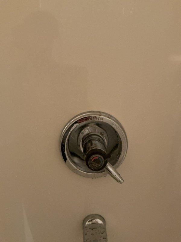 Responded to plumbing leak complaint where upstairs shower was leaking through to the main floor below when in use. Inspected shower control valve assembly and surrounding wall area for signs of water intrusion. Examined chrome trim plate, single-handle lever control, and tub spout fixture, noting aged condition with mineral deposits and water spots indicating ongoing moisture exposure. Assessed valve seals, cartridge, and wall penetration points as potential leak sources. Documented fixture condition and surrounding areas to determine source of water migration to lower level.