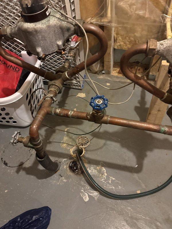 Responded to plumbing leak emergency in basement where water distribution system splits to two meters. Repaired leaking copper union connection at the split point, addressing significant corrosion and oxidation on aged copper piping. Additionally, repaired leaking elbow joint on exterior where plumbing transitions from house through wall to outdoor system, ensuring proper seal and connection integrity at the penetration point. Both leaks were stopped and system restored to proper operation.