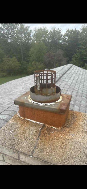 Responded to service call for deteriorated rain cap on shared furnace and water heater flue chimney. Upon roof inspection, found existing cap assembly exhibited severe rust and corrosion on metal base plate and screening components, with visible efflorescence at concrete collar connection indicating moisture intrusion. Removed old rain cap assembly from brick chimney structure and installed new rain cap with proper mesh screening to prevent water entry and debris while maintaining adequate draft for both heating appliances. Verified secure mounting and proper clearances for safe venting operation of 20-year-old furnace and water heater system.