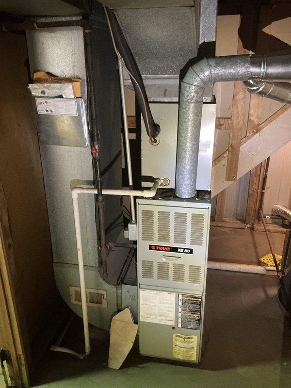 Conducted on-site evaluation for complete HVAC system replacement including 16-year-old air conditioning unit and furnace experiencing operational noise issues upon startup. Assessed existing Trane XE 80 furnace and companion AC system in basement mechanical room, documented equipment specifications, ductwork configuration, and electrical connections. Photographed current installation layout including main supply plenum, refrigerant lines, and existing duct transitions to provide accurate replacement system specifications and installation requirements for comprehensive furnace and air conditioner upgrade estimate.