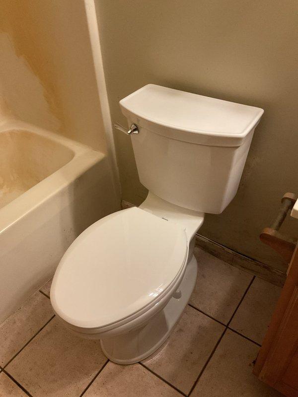 Completed toilet replacement in residential bathroom. Removed existing two-piece toilet and installed new white porcelain two-piece unit with chrome flush lever, ensuring proper positioning, secure mounting, and connection to water supply line. Verified functionality and confirmed no leaks upon completion.