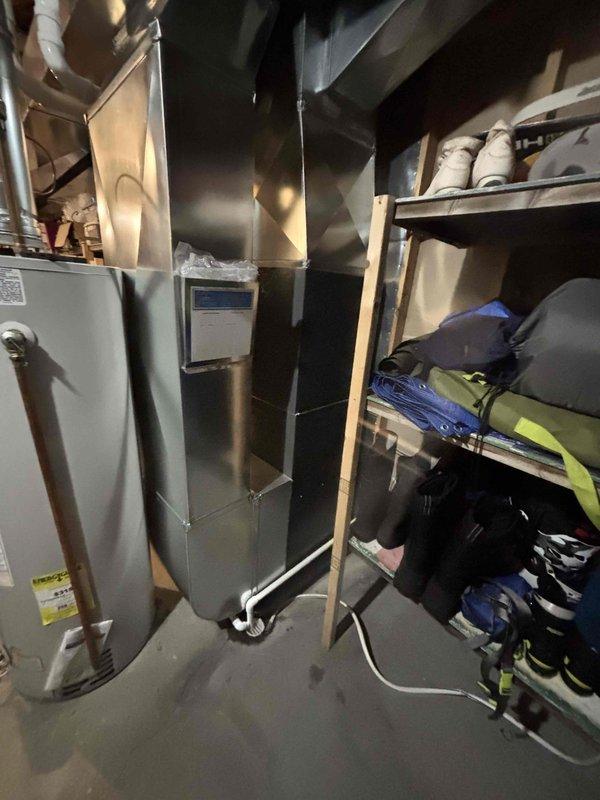 Completed full installation of residential HVAC system including new furnace and air conditioning unit in basement mechanical room. Installed dark-colored high-efficiency furnace with proper white PVC venting routed vertically through structure. Mounted gray metal air handler unit adjacent to furnace with metallic supply ductwork connections. Installed system monitoring and control device with operational indicators at base of equipment. Secured all PVC piping with appropriate brackets and straps to ensure code-compliant installation. Verified all electrical connections, tested system operation, and confirmed proper airflow through ductwork. System powered on successfully with all safety controls and monitoring devices functioning as designed.