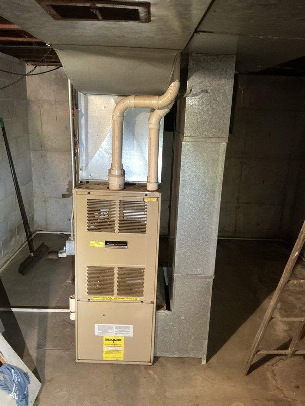 Completed estimate for replacement of aging but operational furnace and air conditioning system. Inspected existing equipment in basement mechanical room, including vertical furnace unit with front-mounted ventilation grilles and PVC exhaust piping, along with associated ductwork in confined mechanical space above. Documented current system configuration through photographs showing galvanized metal supply and return ductwork, cylindrical ventilation components, and overall equipment condition to provide accurate replacement recommendations for updated HVAC system.