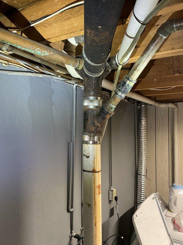 Conducted comprehensive plumbing assessment in unfinished basement to provide project estimate for pipe replacement. Documented existing plumbing infrastructure including aging cast iron drain lines, copper supply piping with visible corrosion and green patina, deteriorating pipe insulation, and mixed-material pipe connections at main junction points. Identified vertical drain pipe with significant rust staining and discoloration requiring replacement. Photographed all plumbing systems, pipe conditions, and access points to support detailed project estimate for complete pipe replacement work.