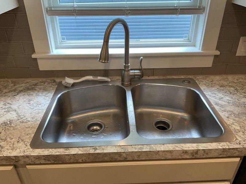 Responded to service call for drain backflow affecting both basins of kitchen double sink. Upon inspection, identified blockage in shared drain line causing water to back up into both sink compartments. Cleared obstruction from main drain line beneath sink cabinet, restoring proper drainage flow through P-trap assembly and disposal connection. Tested both basins under full water flow to verify complete drainage function and confirmed no further backflow issues. System operating normally upon completion.
