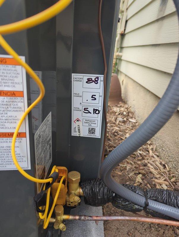 Completed full air conditioning system replacement at residential property. Removed existing outdoor condensing unit and installed new Amana outdoor unit adjacent to building on mulch bed near gas meter. Performed refrigerant line connections using brass fittings and copper piping with proper insulation, verified all connections secure and leak-free. Connected electrical conduit and drain line, applied service identification labels showing system specifications and refrigerant charge information. System tested and operational upon completion.